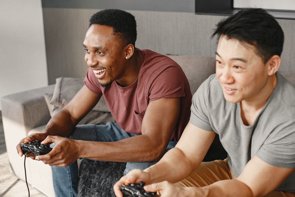 Two friends joyfully playing video games indoors on a cozy couch.